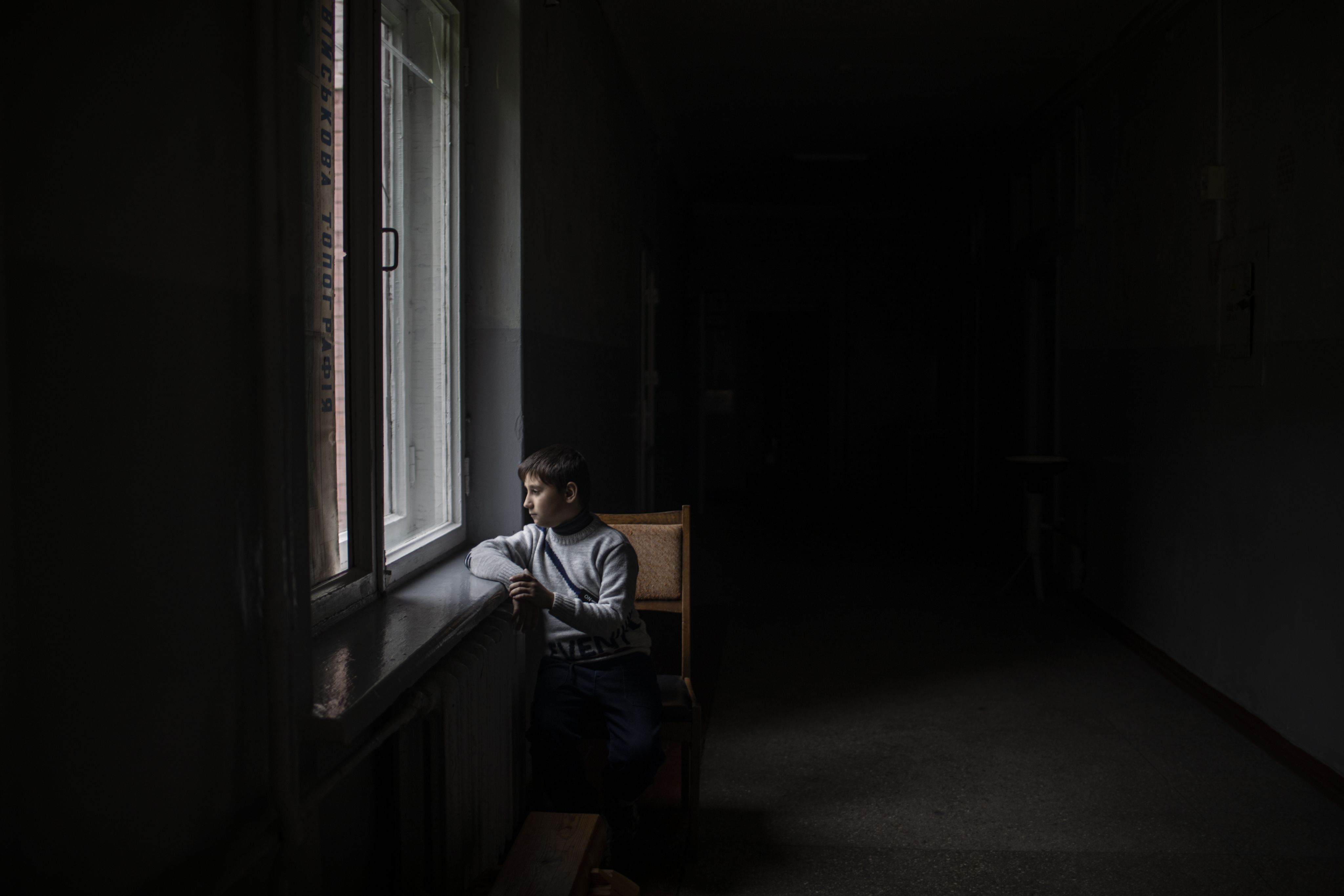 Misha sits in a dark room looking out of a window in a school.