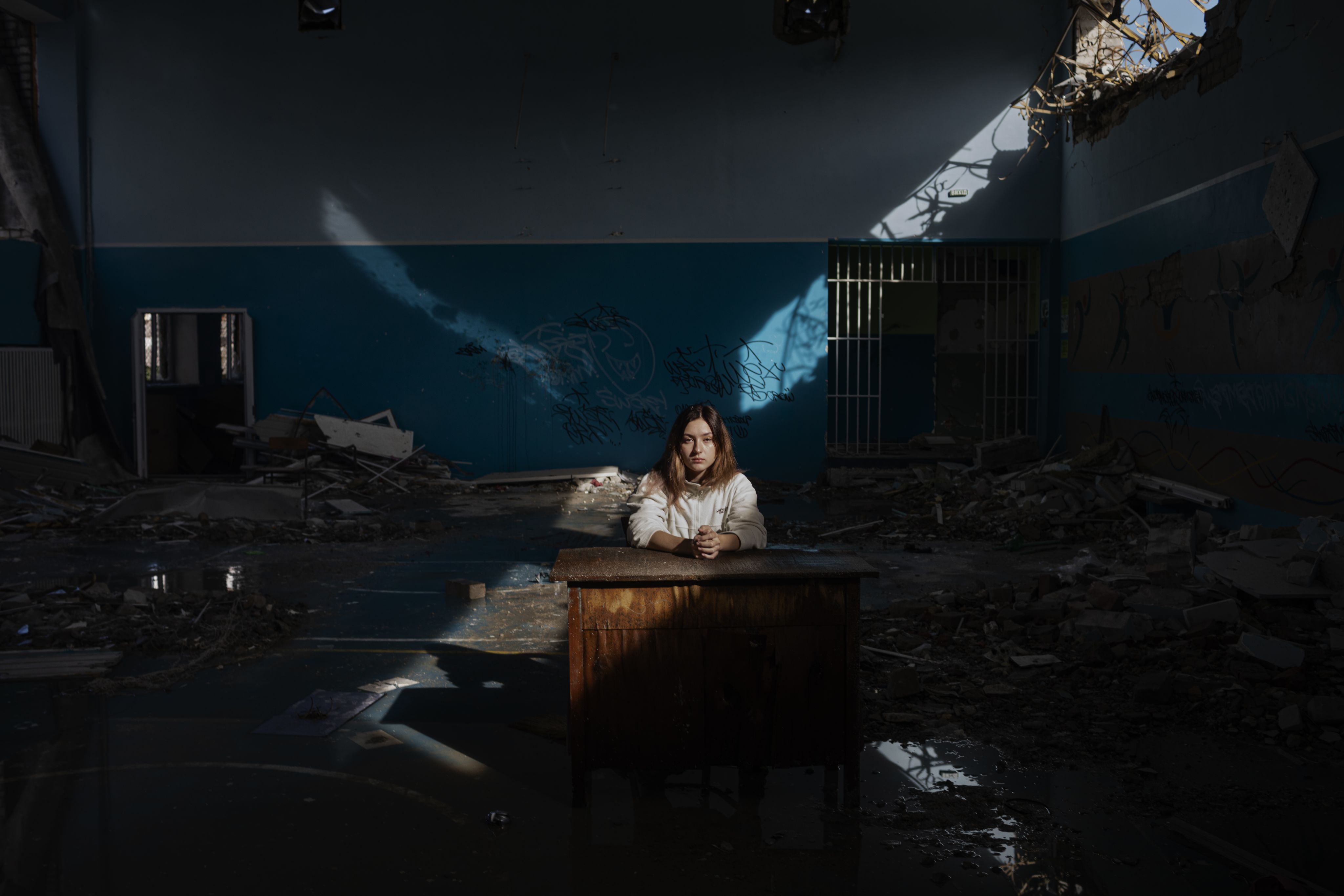 A child sits at a desk in the remains of a classroom that has been badly damaged during the war.